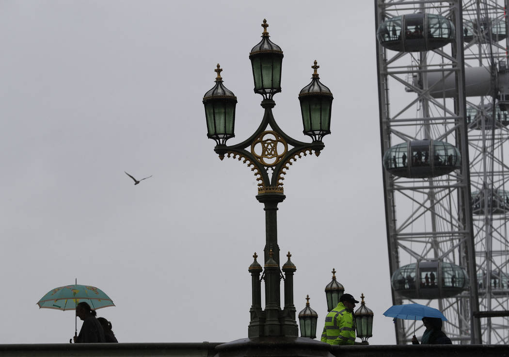 Tourists holding umbrellas pass a policeman standing on Westminster Bridge over the River Thame ...