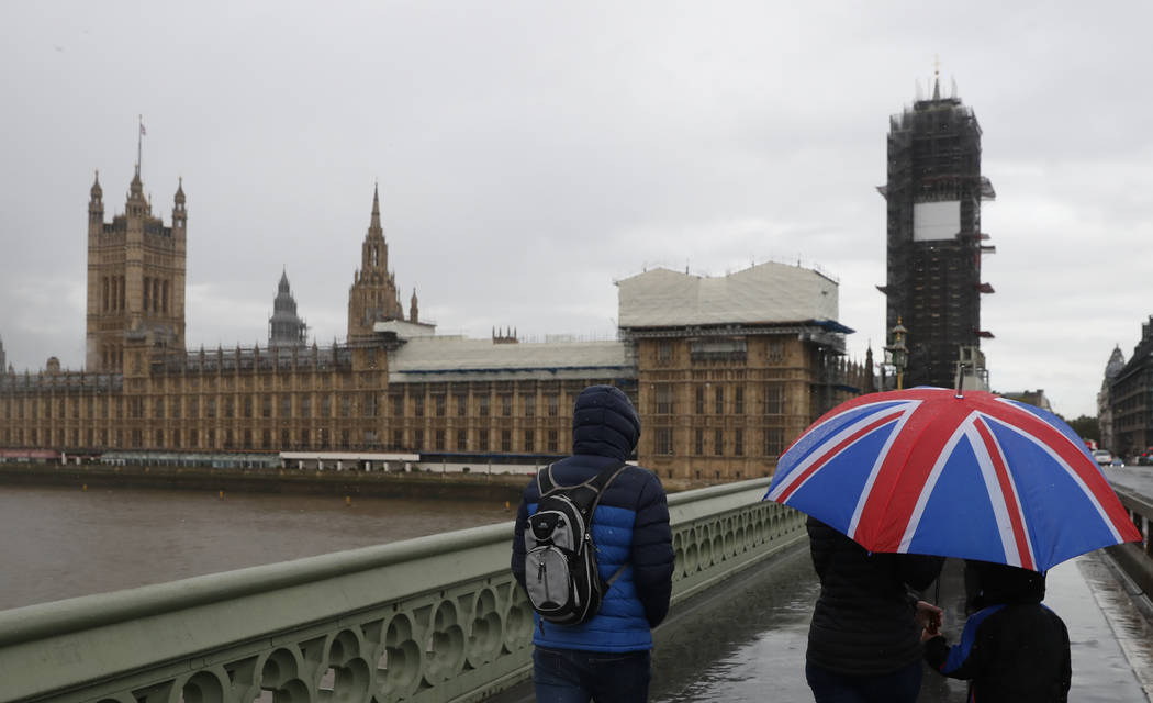 Tourists sheltering underneath a British Union flag umbrella walk across Westminster Bridge in ...