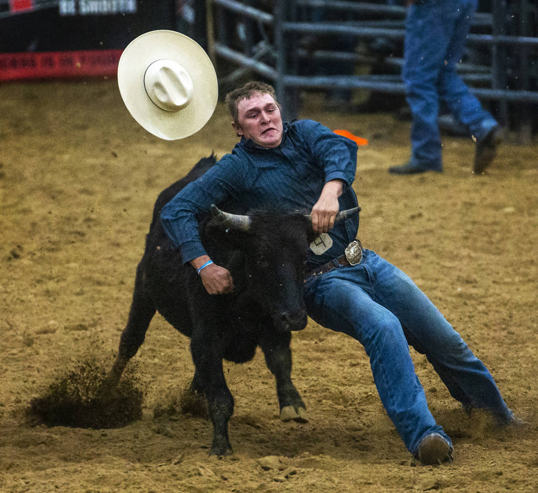 Steer wrestler Tyler Byrne loses his hat but holds onto the steer during the first round of the ...
