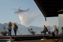 Firefighters watch as a helicopter drops water in a wildfire in the Pacific Palisades area of L ...