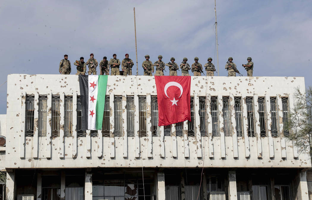 Turkish soldiers, right, and Turkey-backed opposition fighters stand atop a building next to th ...