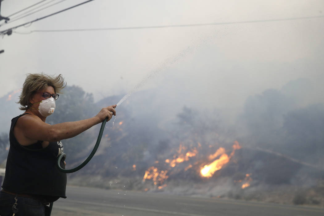 Patricia Dennison uses a hose to try to stop an advancing wildfire from affecting her business, ...