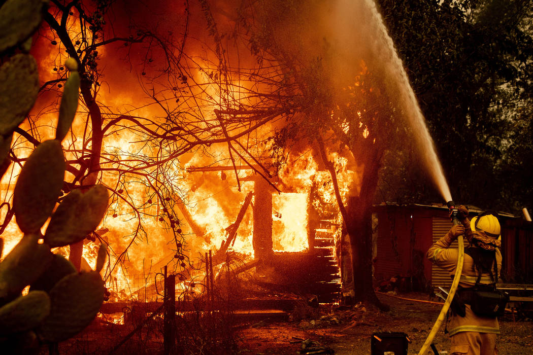 A firefighter sprays water on a burning home as the Kincade Fire burns through the Jimtown comm ...