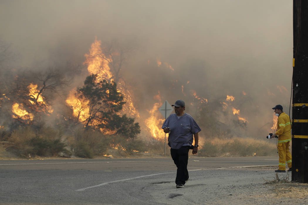 A man walks along Sierra Highway as flames from a wildfire overtake a hillside Thursday, Oct. 2 ...