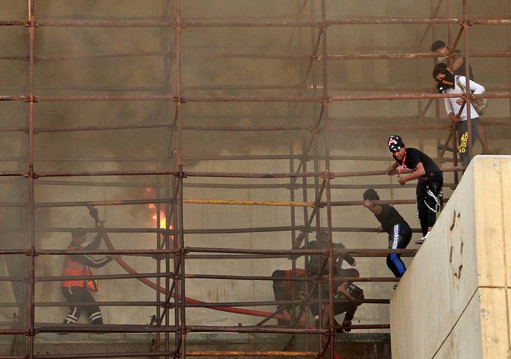 Anti-government protesters escape from a burning building during a demonstration in Baghdad, Ir ...