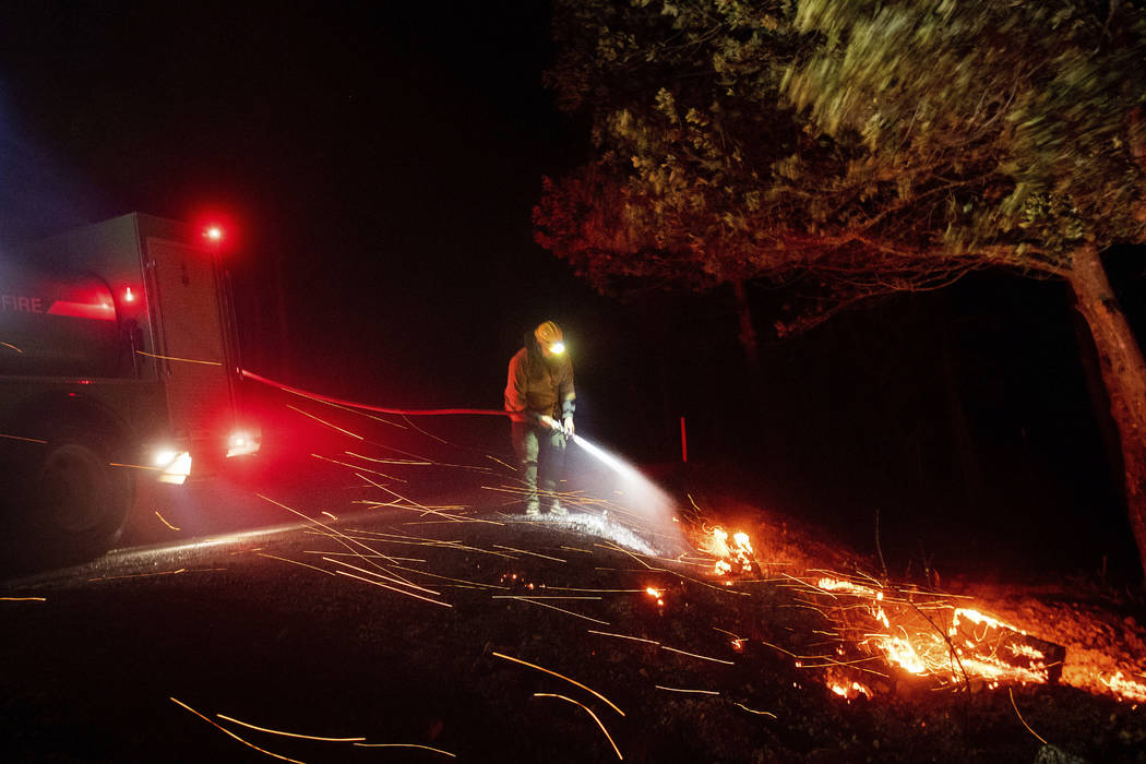 A firefighter battling the Kincade fire extinguishes a hot spot as strong winds send embers fly ...
