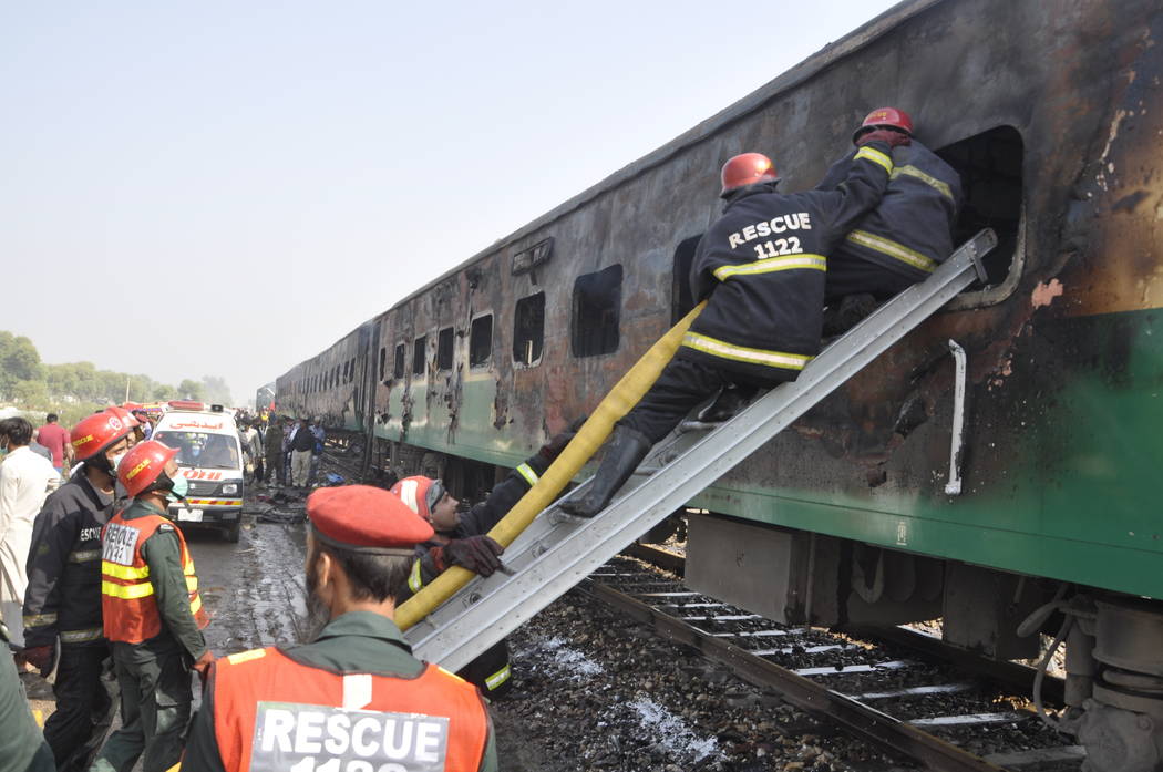 Rescue workers look for survivors following a train damaged by a fire in Liaquatpur, Pakistan, ...