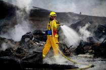 A firefighter sprays water on a leveled home as the Hillside Fire burns in San Bernardino, Cali ...