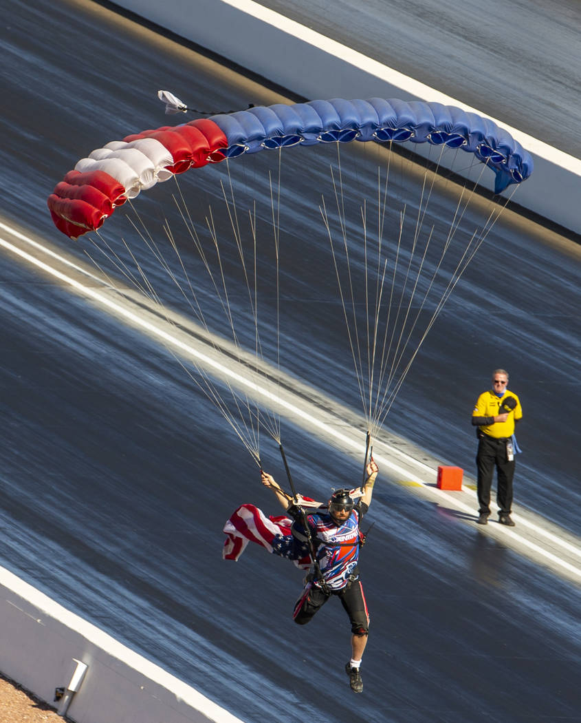 A skydiver delivers the American flag before the National Anthem during the Dodge NHRA National ...
