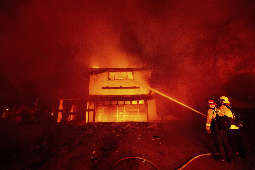 A firefighter sprays water on a scorched home as the Hillside Fire burns in San Bernardino, Cal ...