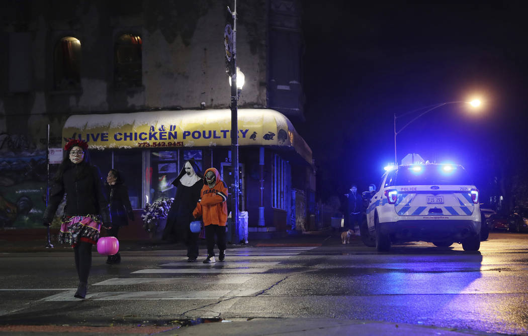 Trick-or-treaters walk past a crime scene in the 3700 block of West 26th Street, where a 7-year ...