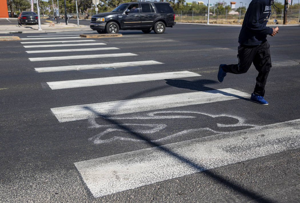 A pedestrian crosses chalk outlines freshly painted by the Las Vegas Fire Department at the int ...