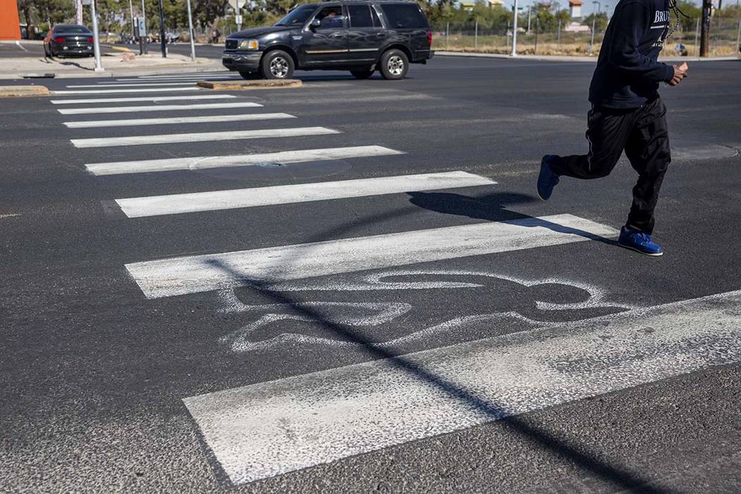 A pedestrian crosses chalk outlines freshly painted by the Las Vegas Fire Department at the int ...