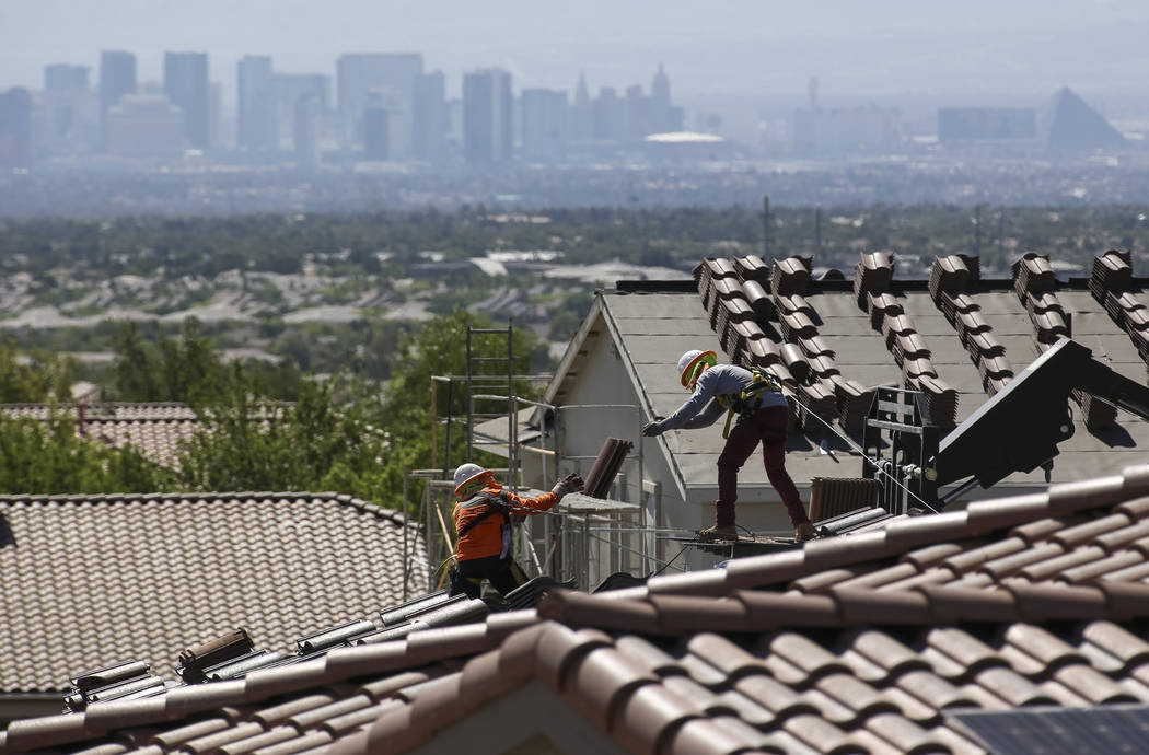 Construction workers set bundles of tile on the roof of an under-construction house in the mast ...