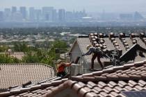 Construction workers set bundles of tile on the roof of an under-construction house in the mast ...