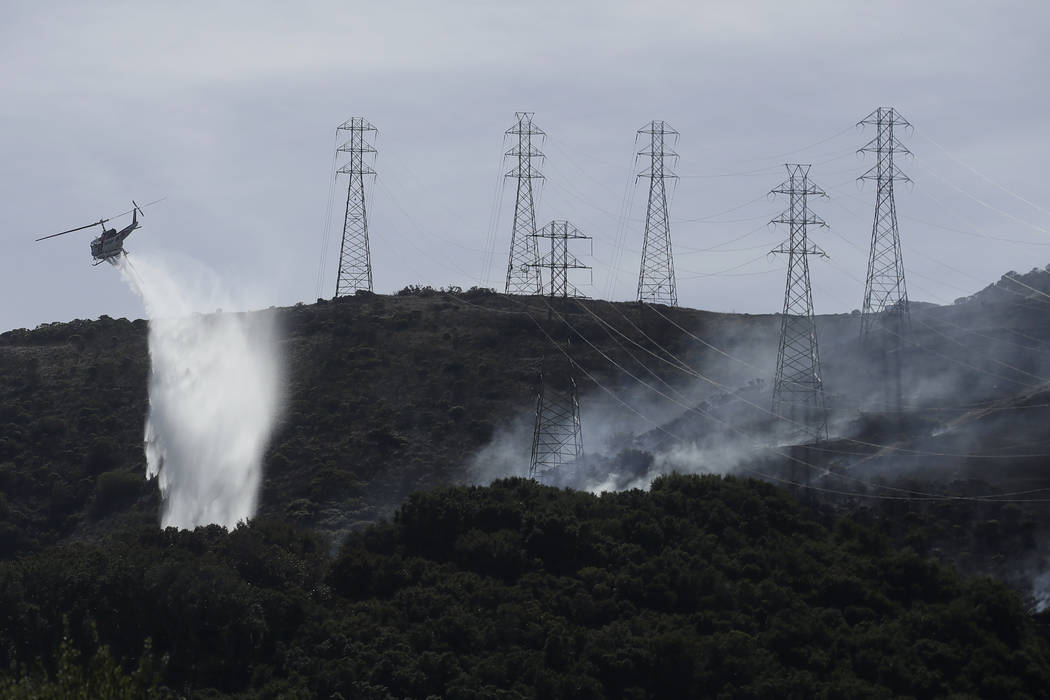 FILE - In this Oct. 10, 2019, file photo, a helicopter drops water near power lines and electri ...