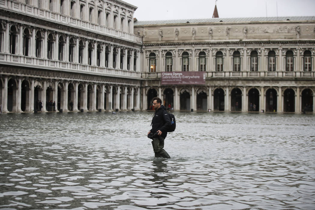 A man holds his cameras as he walks in a flooded St. Mark's Square in Venice, Italy, Friday, No ...