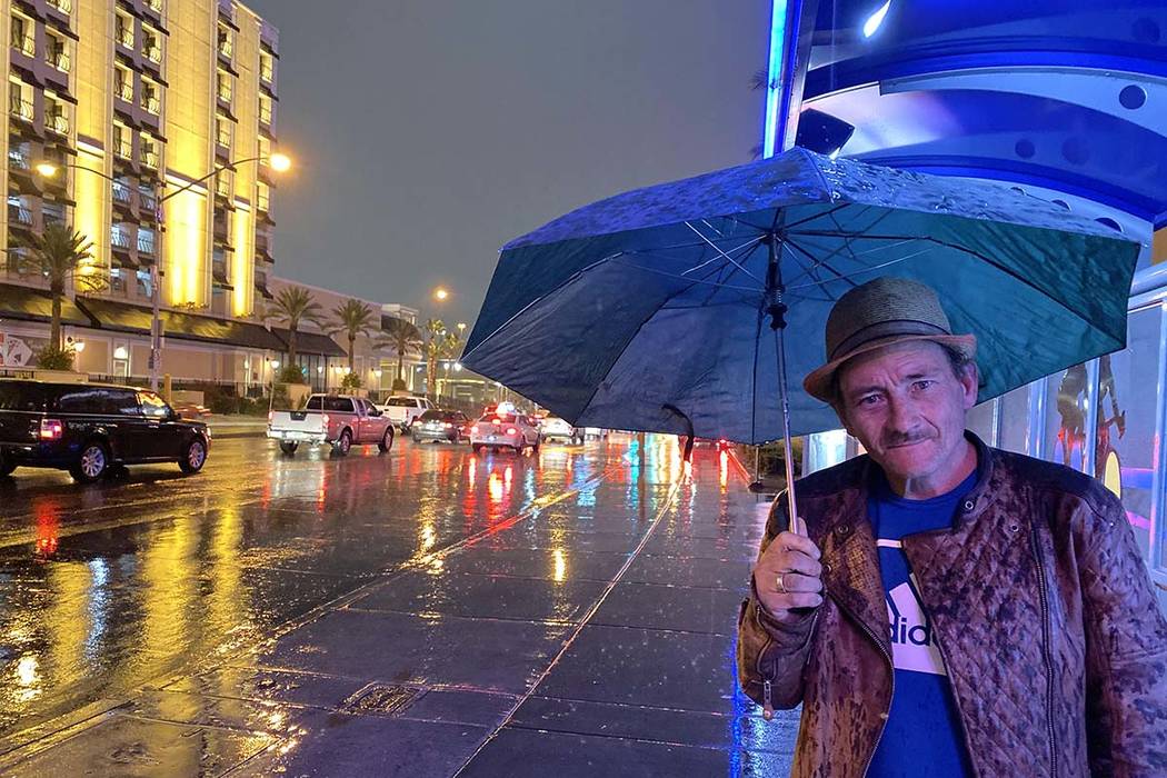 Jimmy James uses an umbrella to protect himself from rain as he waits for a bus about 5 a.m. We ...