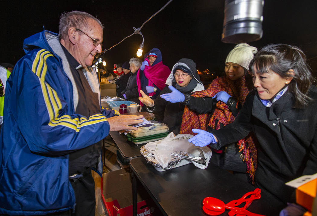 Father John McShane, left, passes out prayer books to some of the volunteers serving meals duri ...