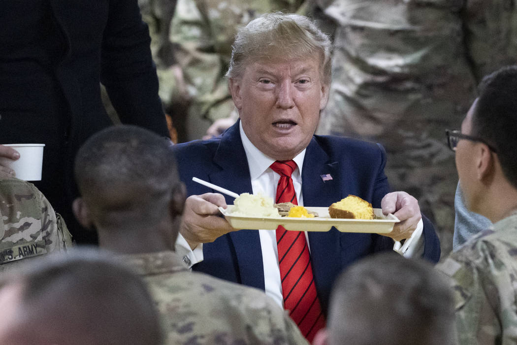 President Donald Trump holds up a tray of Thanksgiving dinner during a surprise Thanksgiving Da ...
