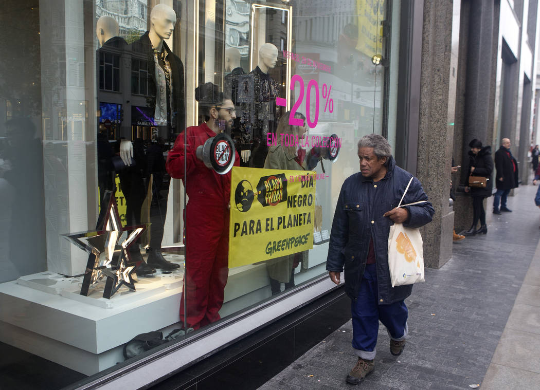 A woman walks past past Greenpeace activists standing inside a store window display during a Bl ...