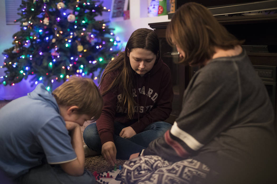 Rebecca Cabral, 14, center, plays a board game with her brother Joseph Cabral, 12, left, and th ...