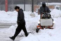 A pedestrian makes their way through a parking lot where snow is being cleared after an overnig ...