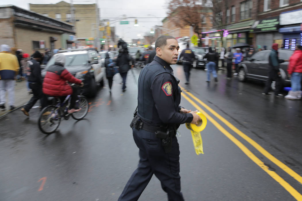 A police officer pushes pedestrians back from the scene of a shooting in Jersey City, N.J., Tue ...
