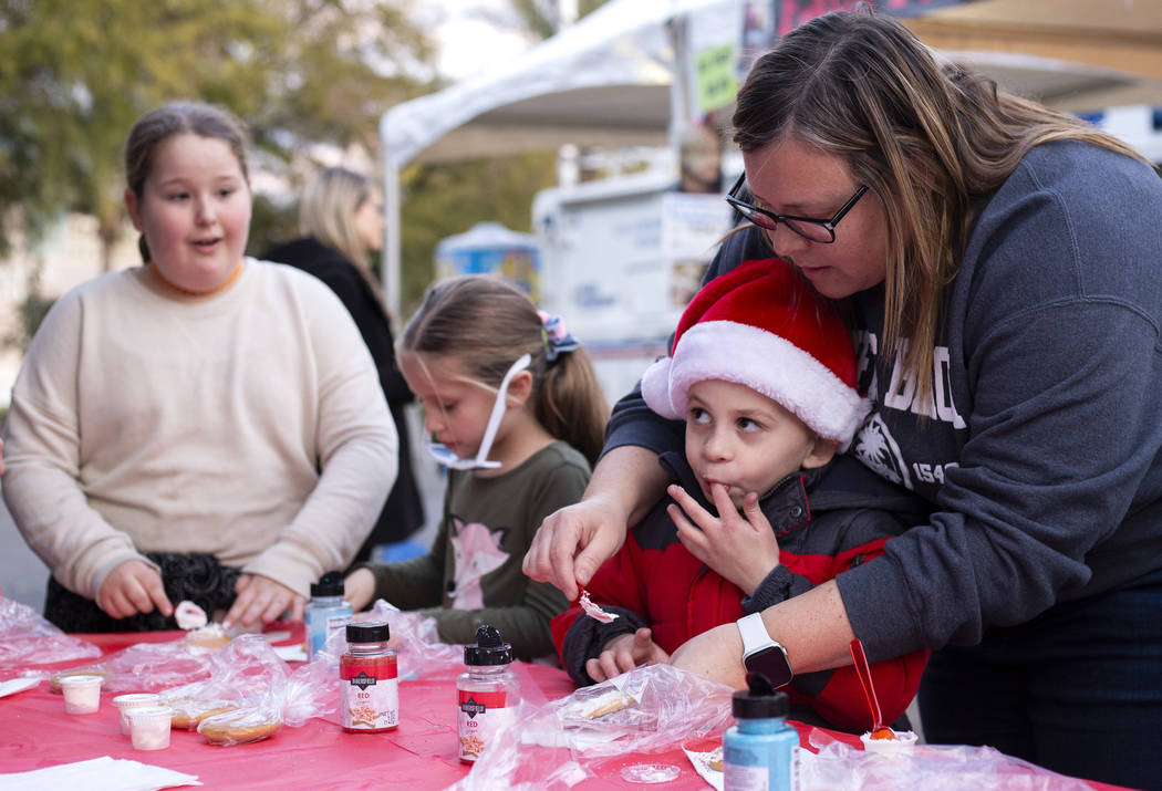Travis Williams, 6, sneaks a bite of frosting as he decorates a cookie with the help of his mot ...