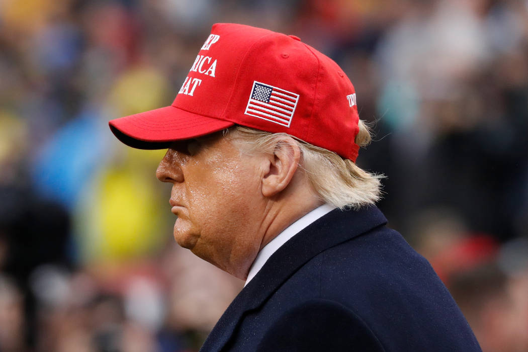President Donald Trump wears a red hat as he stands on the field before the Army-Navy college f ...