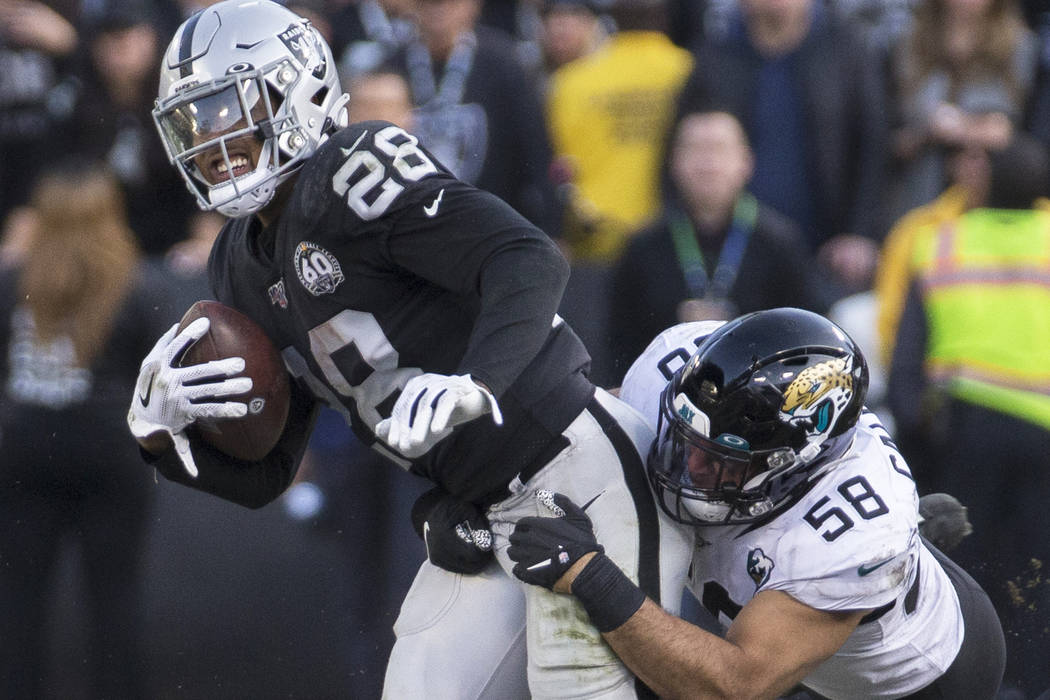 Oakland Raiders running back Josh Jacobs (28) drags Jacksonville Jaguars outside linebacker Aus ...