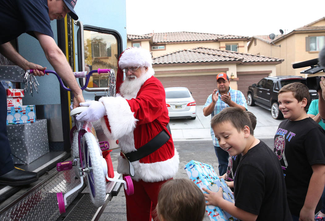 Aria Runyan, 4, left, and her brothers Erick Jr., 8, and Ethan, 10, right, watch as Santa unloa ...