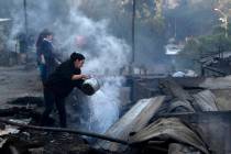 Residents spray water over remains of their homes after a wildfire damaged dozens of houses on ...