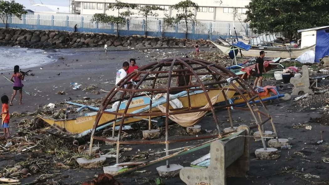 Residents walks beside an outrigger and playground equipment that were damaged by Typhoon Phanf ...