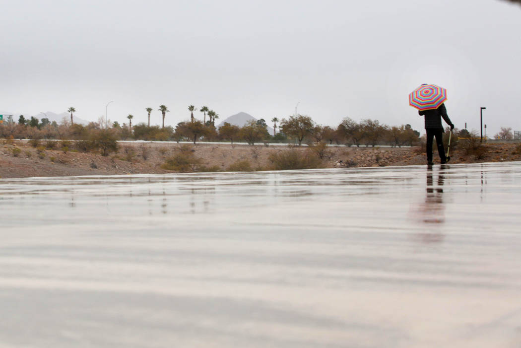 An individual takes a morning walk as the rain falls in the Las Vegas valley on Thursday, Dec. ...