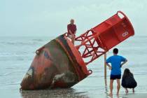 Beachgoers inspect a navigational marker that washed up on the beach last week in New Smyrna Be ...