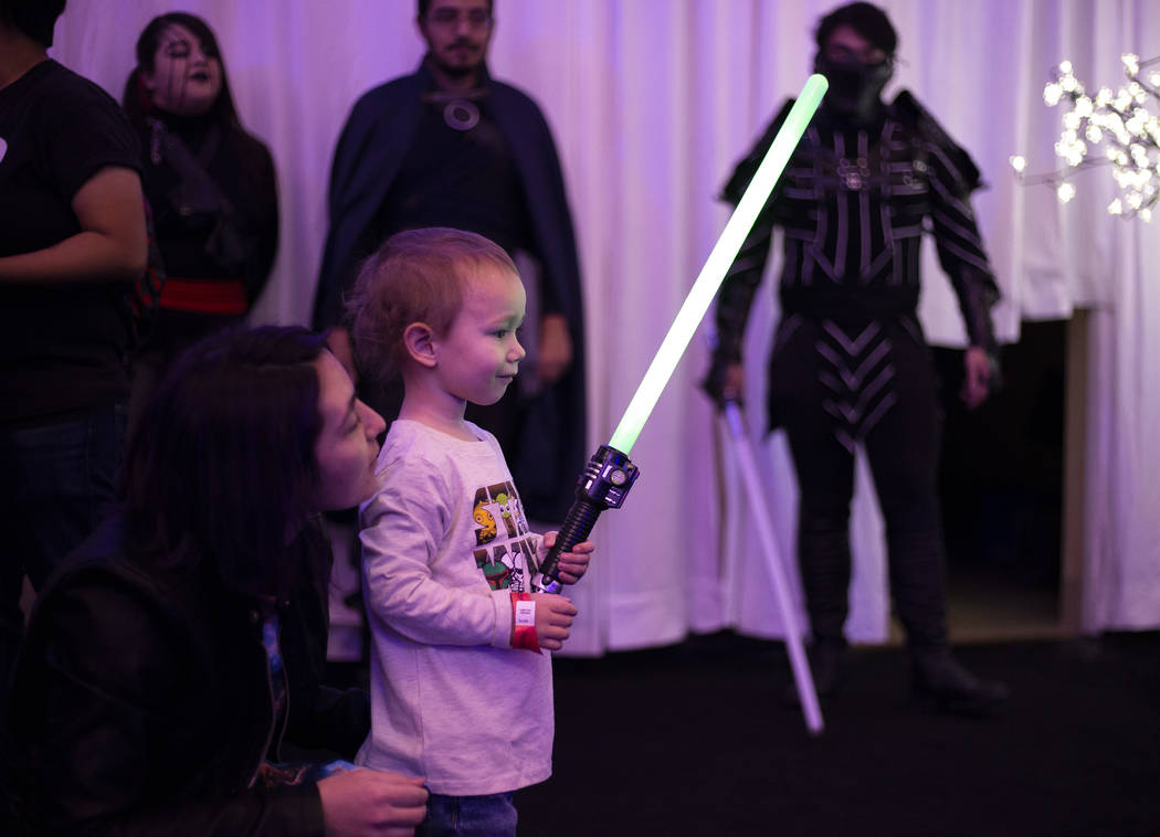Daymien Freeth, 2, is in awe of his light saber as his mom, Theresa Freeth, encourages him at t ...