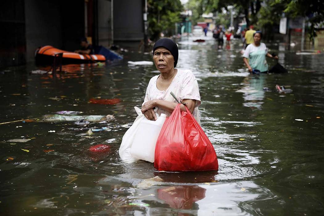 A woman wades flood water in Jakarta, Indonesia, Saturday, Jan. 4, 2020. Monsoon rains and risi ...