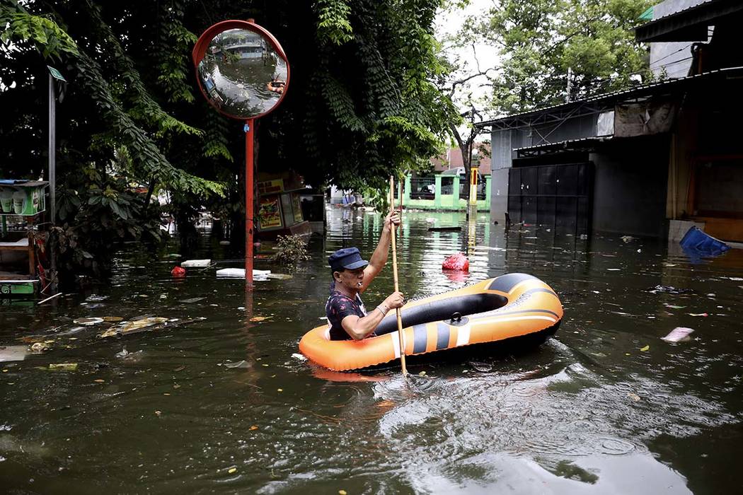 A man navigates an inflatable boat at a flooded neighborhood in Jakarta, Indonesia, Saturday, J ...
