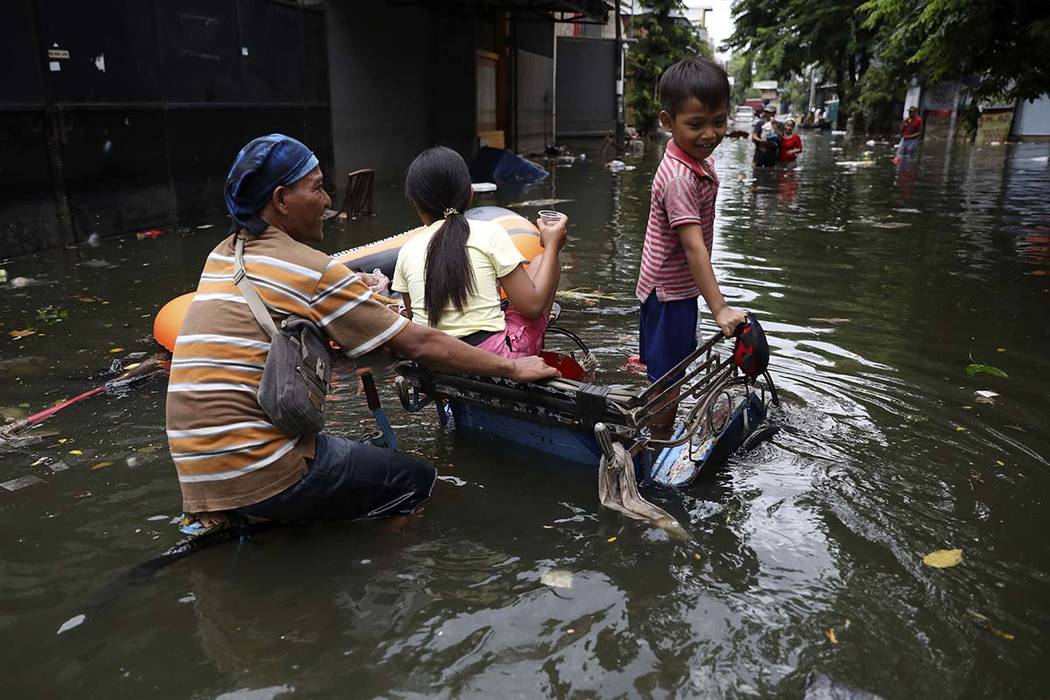 A young boy reacts as he rides on a tricycle with his father and sister at a flooded neighborho ...