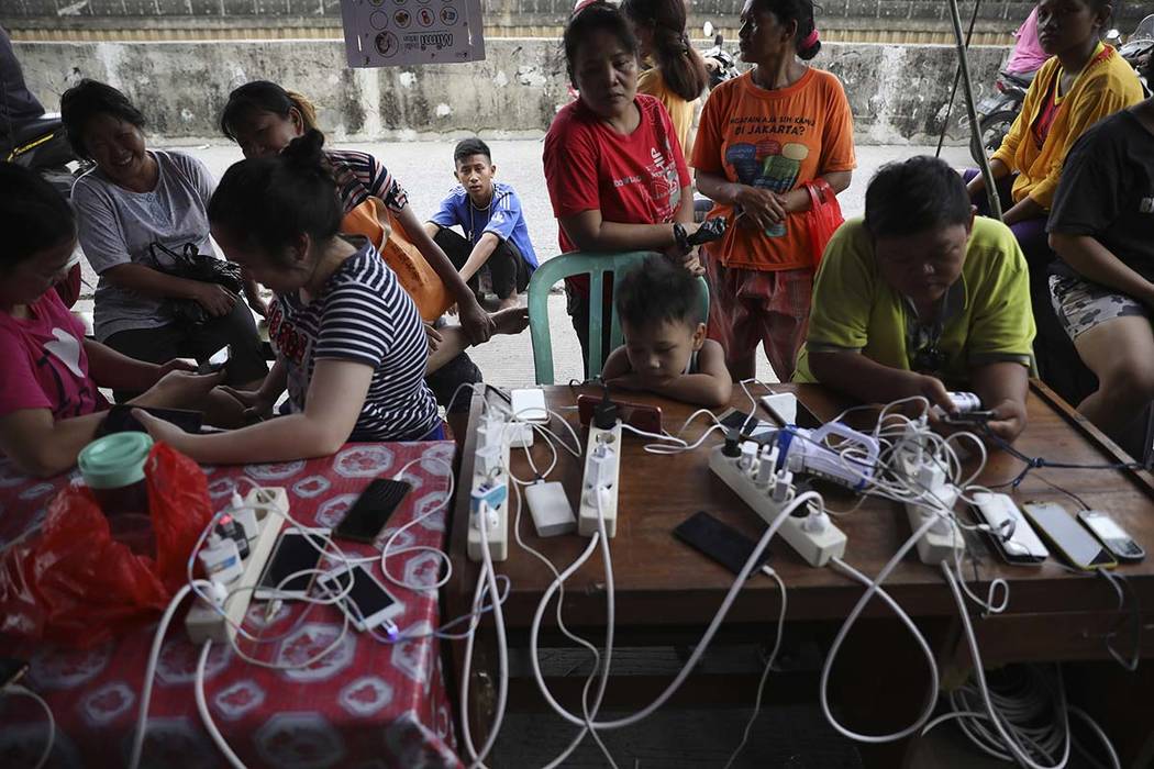 People check their phones at a charging station for those affected by floods in Jakarta, Indone ...