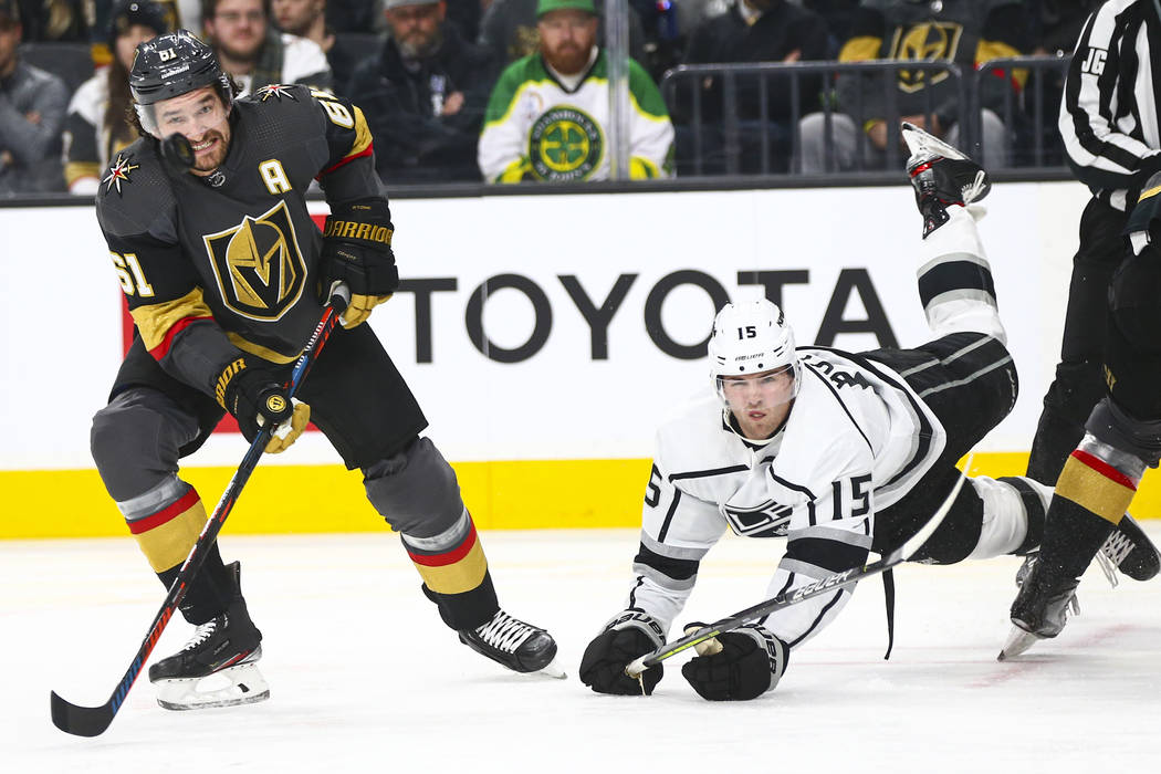 Golden Knights' Mark Stone (61) eyes the puck as Los Angeles Kings' Ben Hutton (15) gets trippe ...