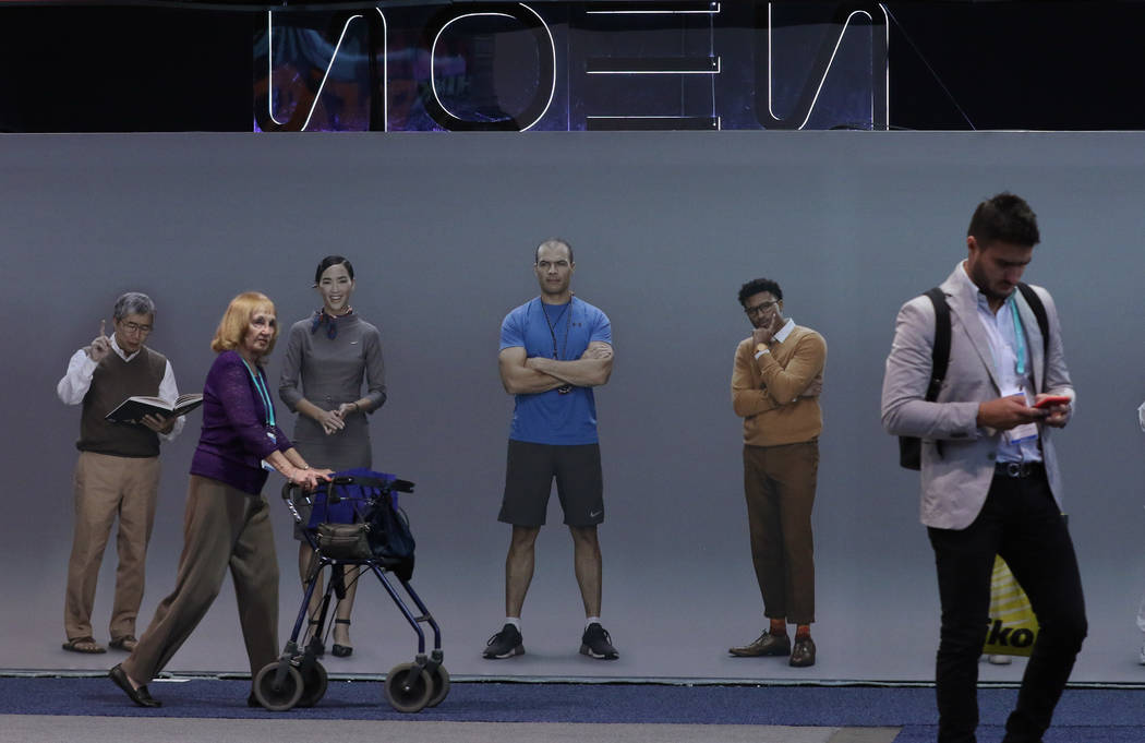 Conventiongoers walk pass Neon's, a computationally created virtual being that looks and behave ...
