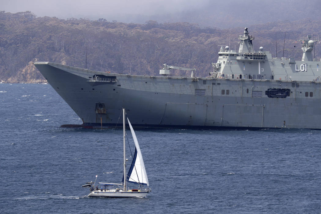 A yacht sails past HMAS Adelaide waiting in the harbor to assist in the wildfire emergency in E ...