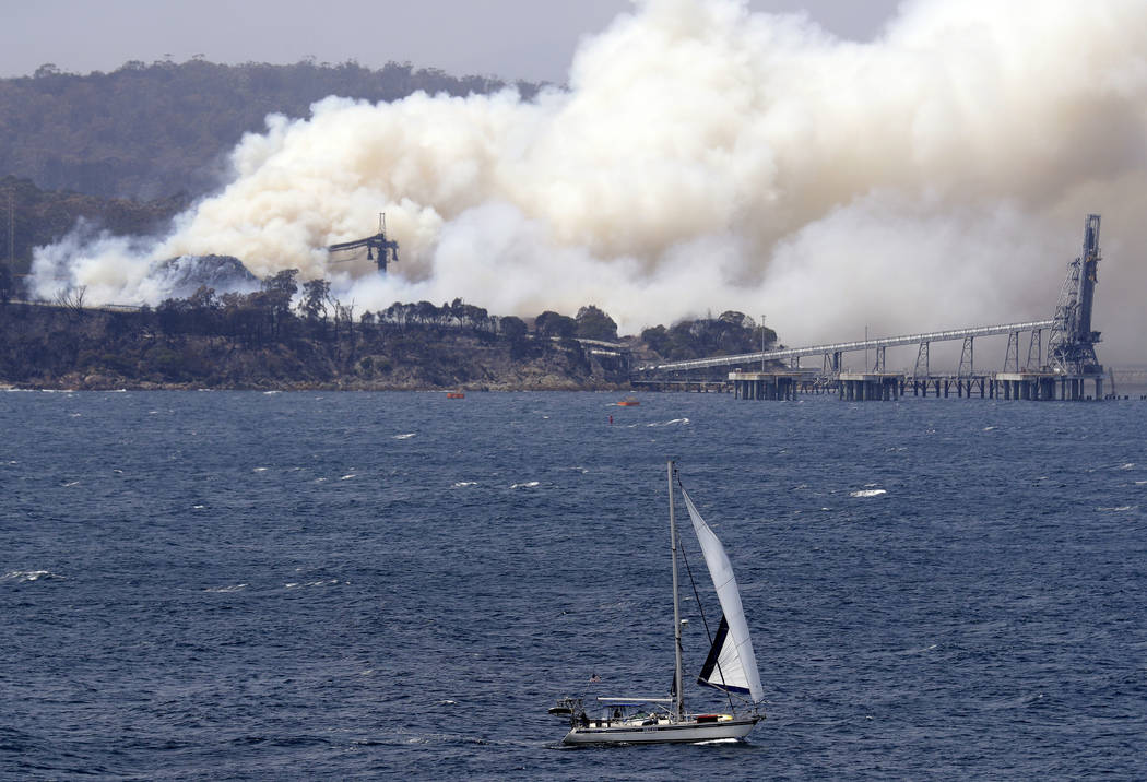 A yacht sails past a burning woodchip mill as the wildfires hits the town of Eden, New South Wa ...