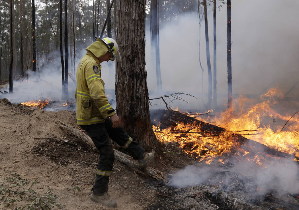 A firefighter kicks at a log while helping to build a containment line at a fire near Bodalla, ...