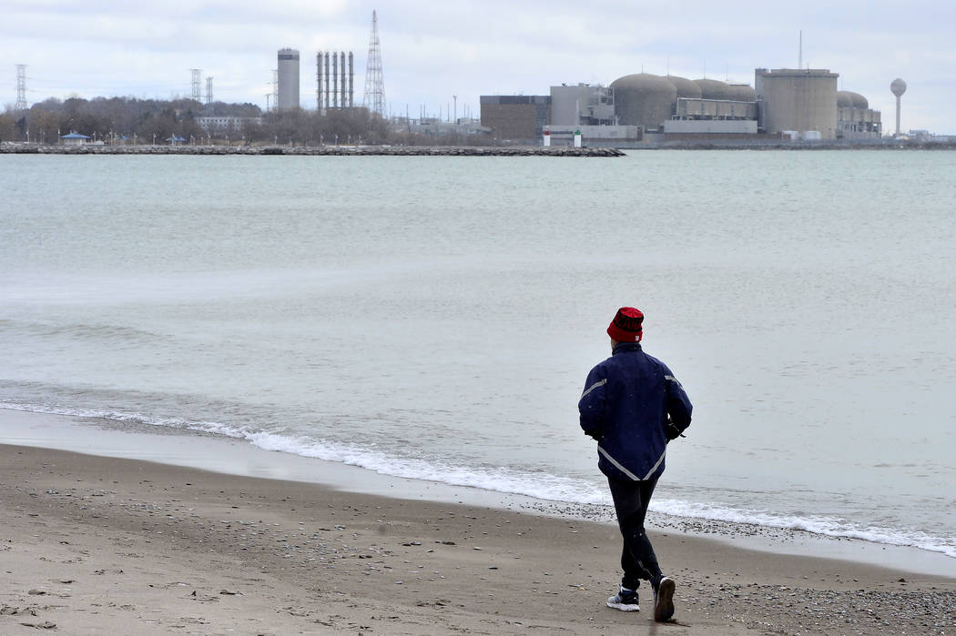 A jogger runs along the beach past the Pickering Nuclear Generating Station, in Pickering, Onta ...