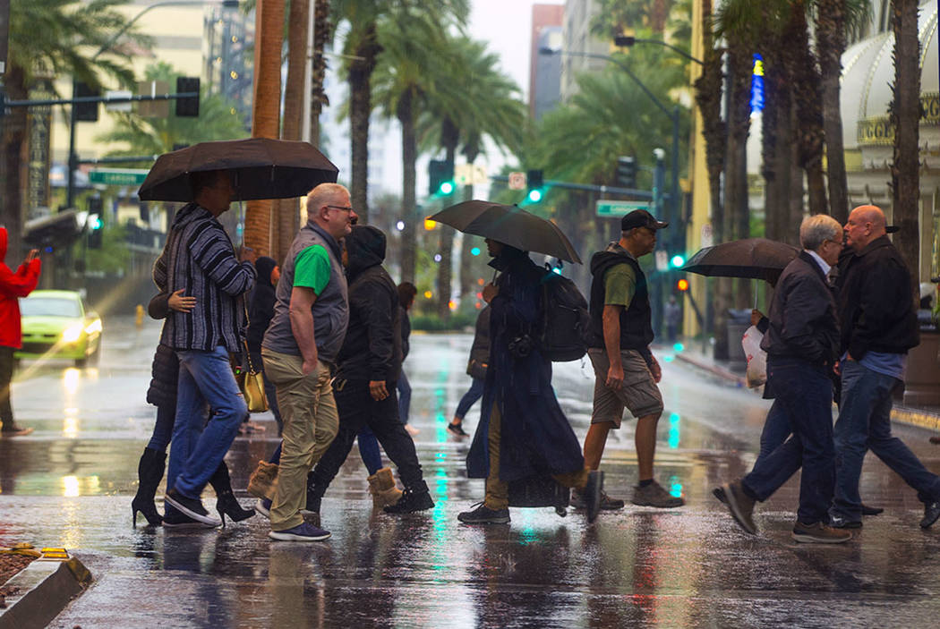 People cross the street on a rainy day about the Fremont Street Experience and South 3rd Street ...