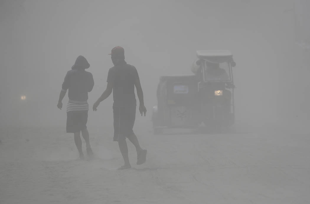 Residents walk in a cloud of ash as Taal Volcano continues to spew ash on Monday Jan. 13, 2020, ...