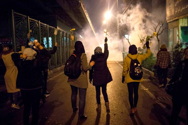 In a photograph taken Saturday, Jan. 11, 2020, protesters hold flowers as tear gas fired by pol ...